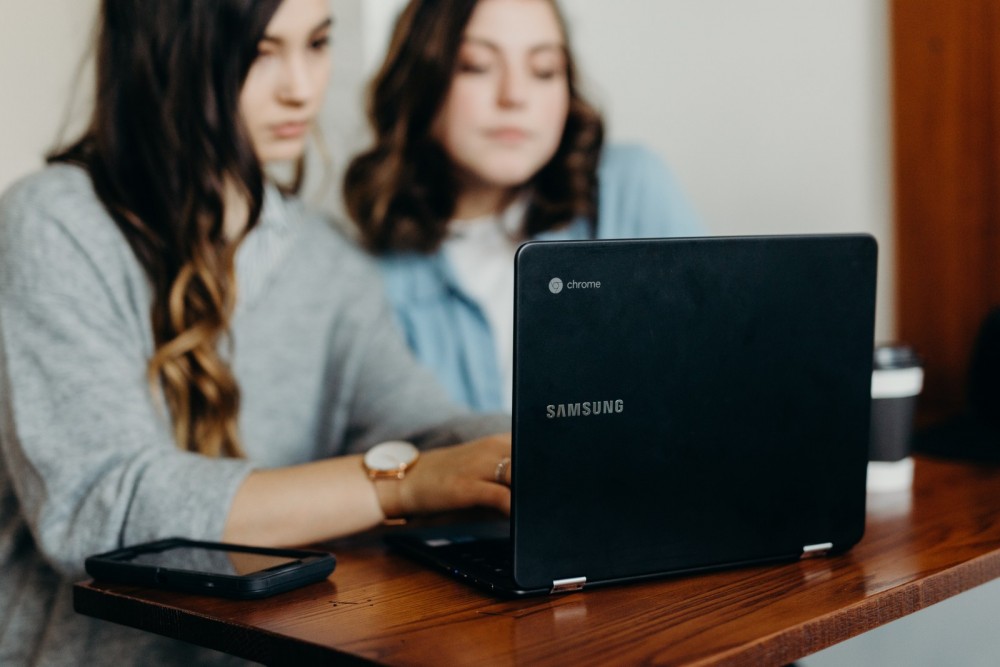 Zwei Frauen sitzen vor einem Laptop.