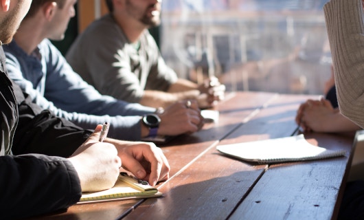 4 Menschen sitzen an einem Tisch und diskutieren gemeinsam