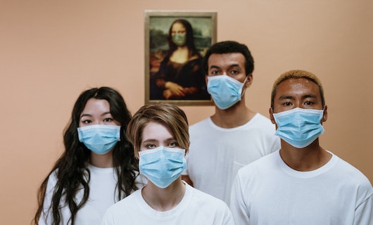 Vier junge Menschen tragen eine OP-Maske und schauen in die Kamera