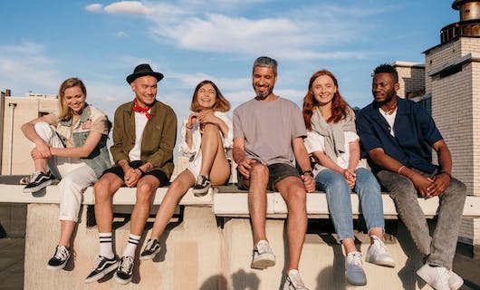 Sechs Junge Menschen sitzen lachend auf einer Mauer