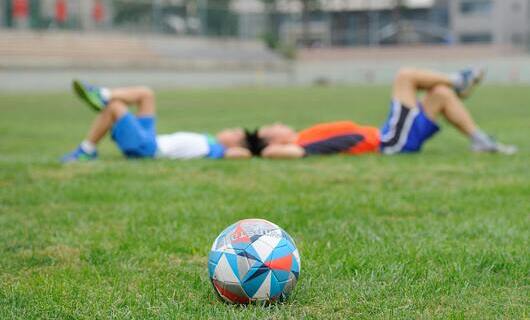 Ein Fußball im Vordergrund, dahinter liegen zwei Kinder im Gras