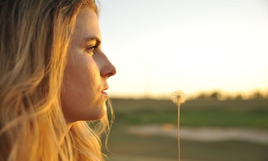 Foto: Jugendliche blickt in den Sonnenaufgang mit einer Pusteblume in der Hand