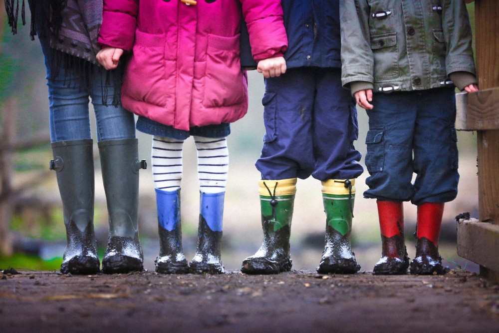 Vier Kinder tragen Gummistiefel und stehen in der Natur.