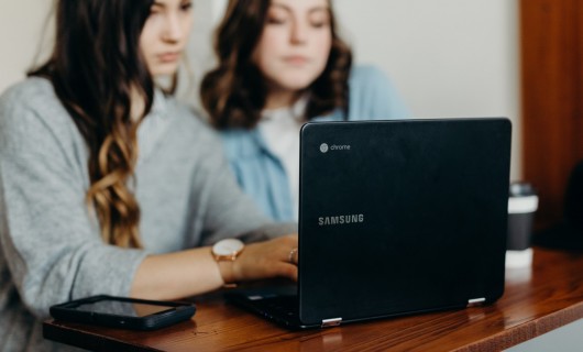 Zwei Frauen sitzen vor einem Laptop.