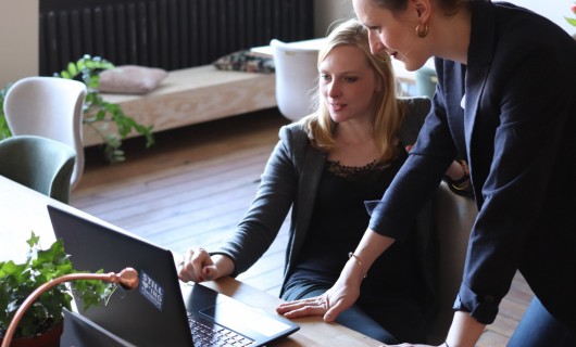 Zwei Frauen schauen zusammen auf einen Laptop.