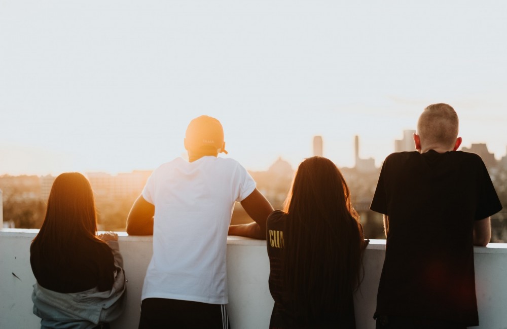 Vier Jugendliche sind von hinten zu sehen und schauen auf eine Stadt. 