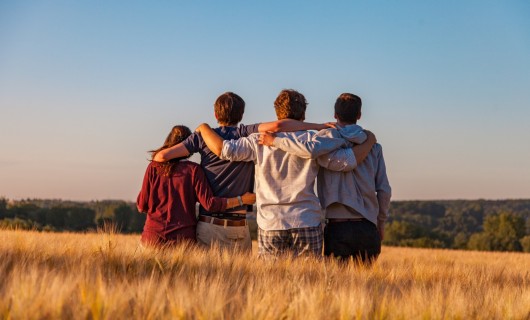 Vier Jugendliche stehen in einem Weizenfeld, es ist nur ihr Rücken zu sehen.
