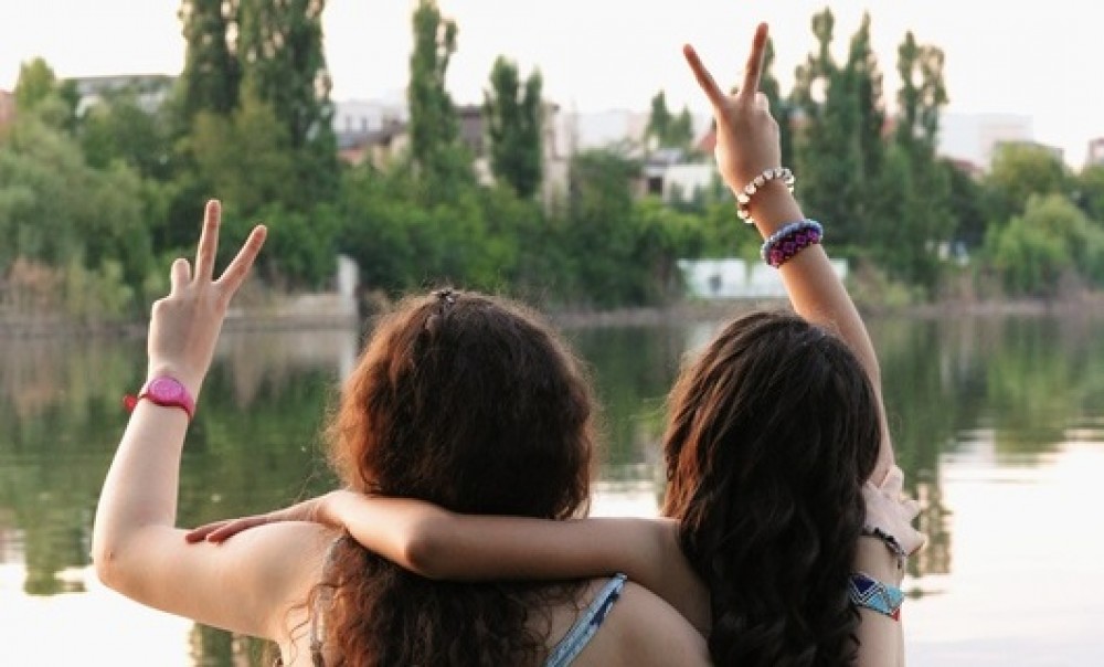 Zwei junge Menschen sitzen am Wasser und machen Peacesymbole mit ihren Händen (Foto: FidesP via pixabay.com)