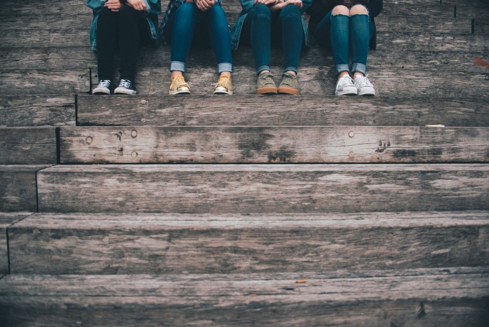 Vier junge Menschen sitzen auf einer Treppe, es sind nur die Beine und Füße zu sehen.