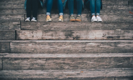 Vier Frauen sitzen auf einer hölzernen Treppe, es sind nur die Beine und Füße zu sehen.