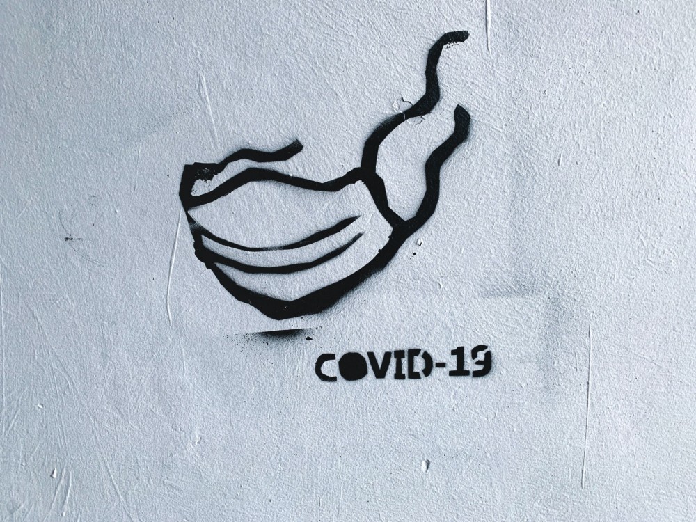 Graffiti auf einer Wand von einem Mundschutz mit der Unterschrift covid 19. 