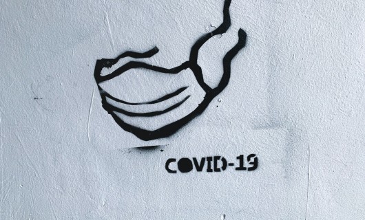 Graffiti auf einer Wand von einem Mundschutz mit der Unterschrift covid 19. 