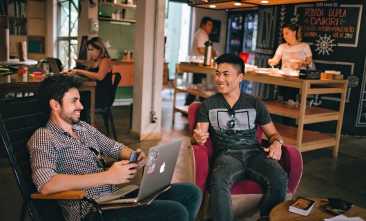 Zwei Männer sitzen in einem Co-Workingspace zusammen und arbeiten an einem Laptop.