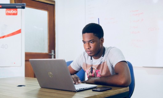 Ein Mann sitzt in einem Seminarraum vor einem Laptop.