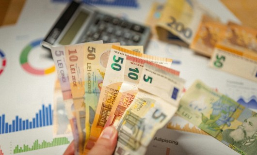 Eine Hand hält verschiedenfarbige Geldscheine, im Hintergrund liegt ein Tschenrechner.