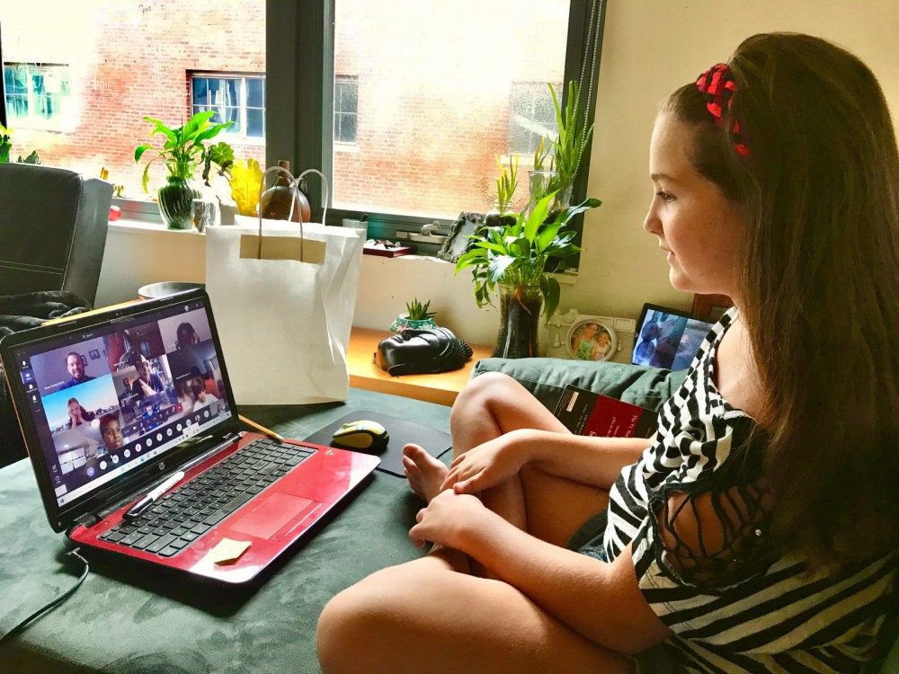 Eine junge Frau sitzt vor ihrem Laptop und nimmt an einer Videokonferenz teil.