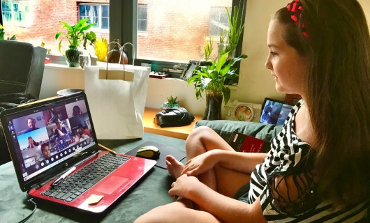 Eine junge Frau sitzt vor ihrem Laptop und nimmt an einer Videokonferenz teil.