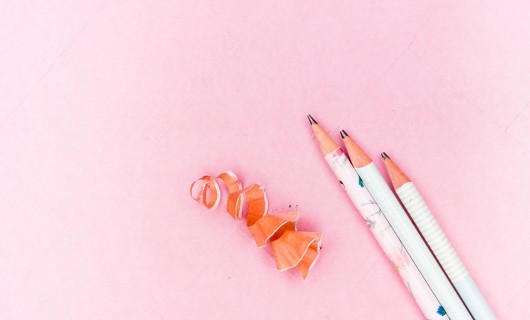 Drei Bleistifte liegen auf rosafarbenem Hintergrund.