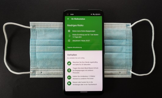 Ein Smartphone zeigt die Corona-Warnapp und liegt auf einer Mund-Nasen-Maske.