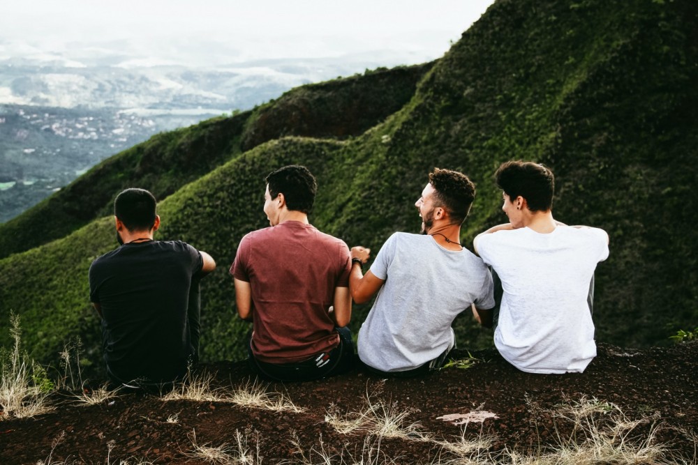 Vier Männer sitzen auf einem Hügel und sind von hinten zu sehen.