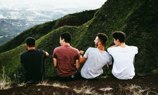 Vier Männer sitzen auf einem Hügel und sind von hinten zu sehen.