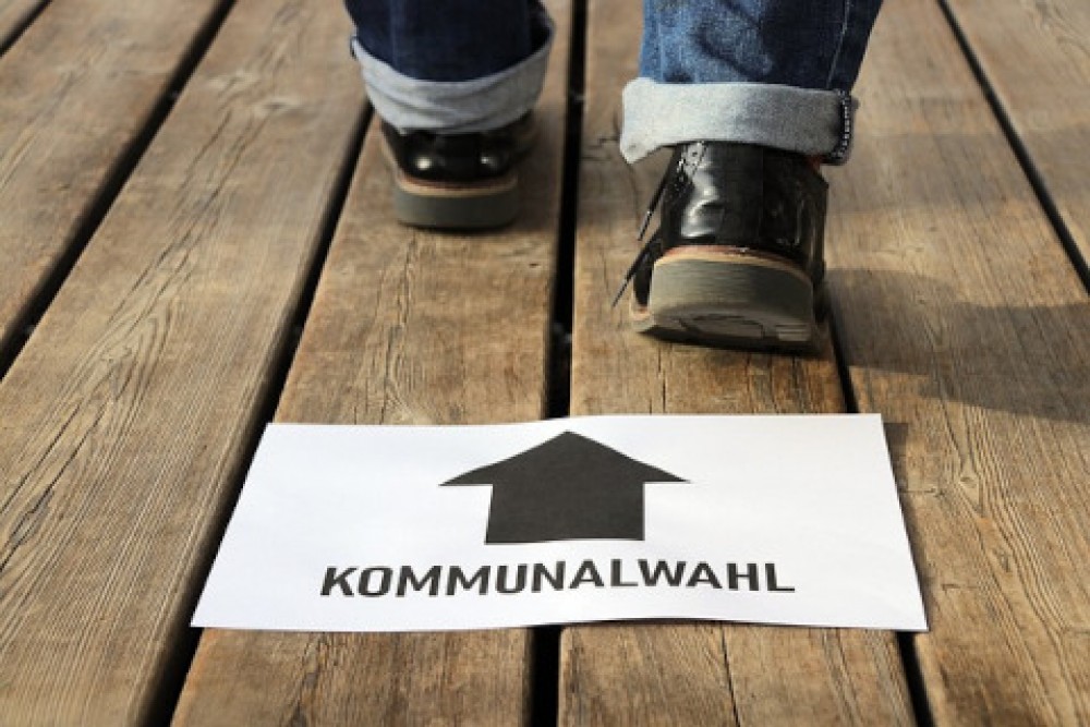 Schild mit Aufschrift &quotKommunalwahlen" vor zwei sich nach vorn bewegenden Füßen