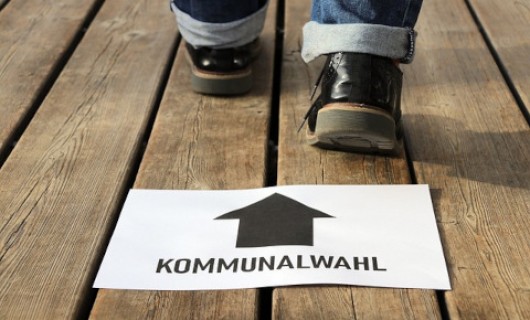 Schild mit Aufschrift &quotKommunalwahlen" vor zwei sich nach vorn bewegenden Füßen