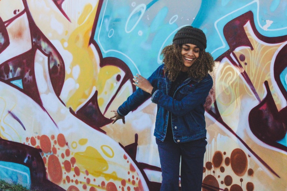 Eine Frau steht vor einer Grafitiwand und lacht.