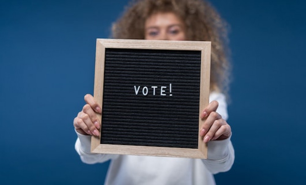 Eine Frau hält eine Tafel mit dem Slogan &quotVote!" in die Kamera. Foto: cottonbro studio via pexels.com