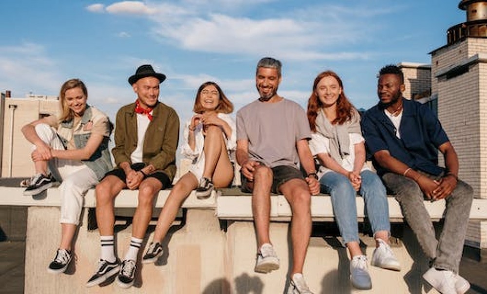 Sechs Junge Menschen sitzen lachend auf einer Mauer