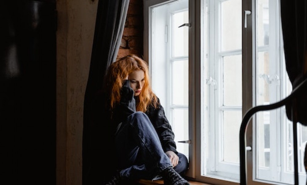 Junge Frau sitzt traurig am Fenster