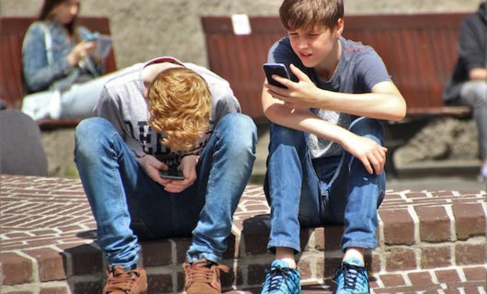 2 Jungen sitzen mit Smartphones in der Hand auf einem Bordstein