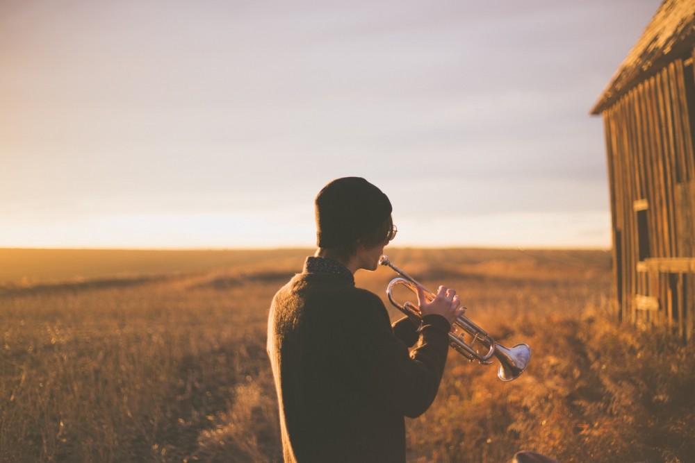 Ein junger Mann steht auf einem Feld und spielt Trompete.