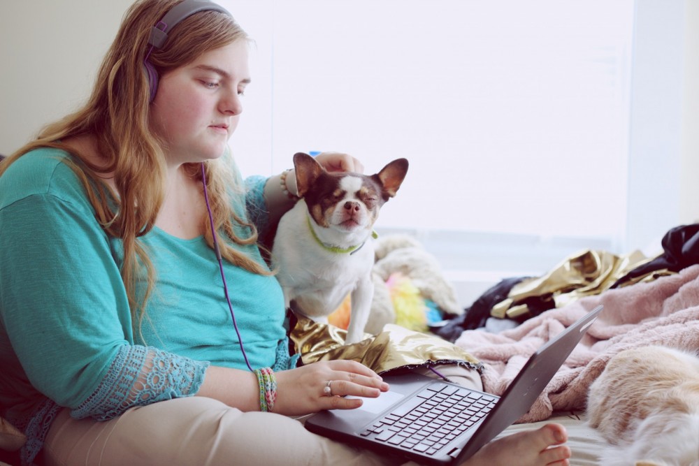 Eine Frau und ein Hund sitzen vor einem Laptop, die Frau trägt Kopfhörer.