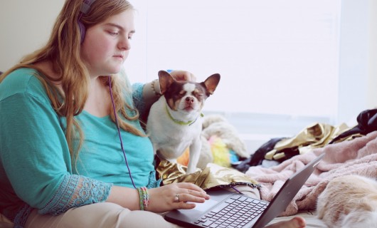 Eine Frau und ein Hund sitzen vor einem Laptop, die Frau trägt Kopfhörer.