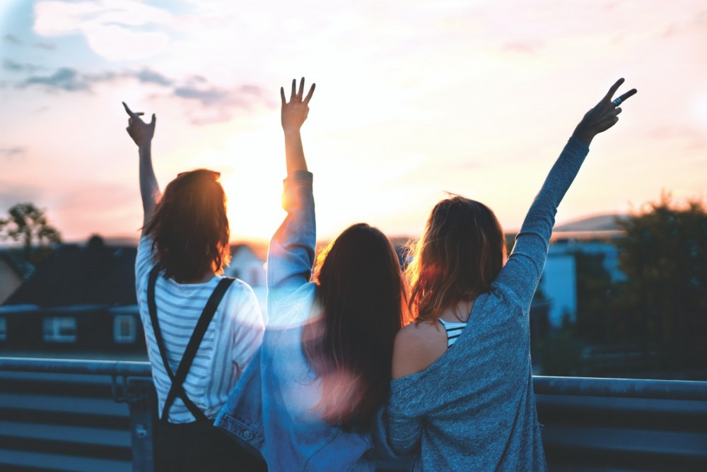 Drei Frauen sind von hinten zu sehen, sie strecken alle ihre Hände in die Luft.