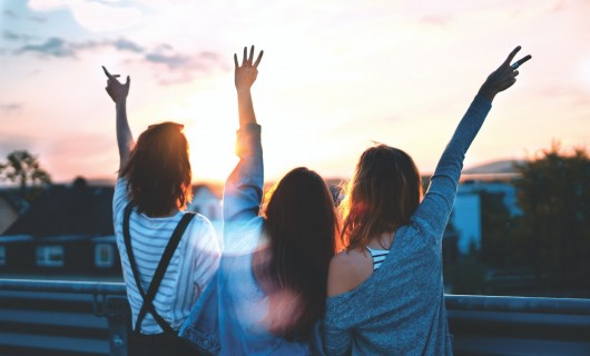 Drei Frauen sind von hinten zu sehen, sie strecken alle ihre Hände in die Luft.