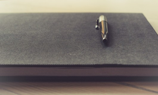 Ein Stift liegt auf einem dunklen Notizbuch.