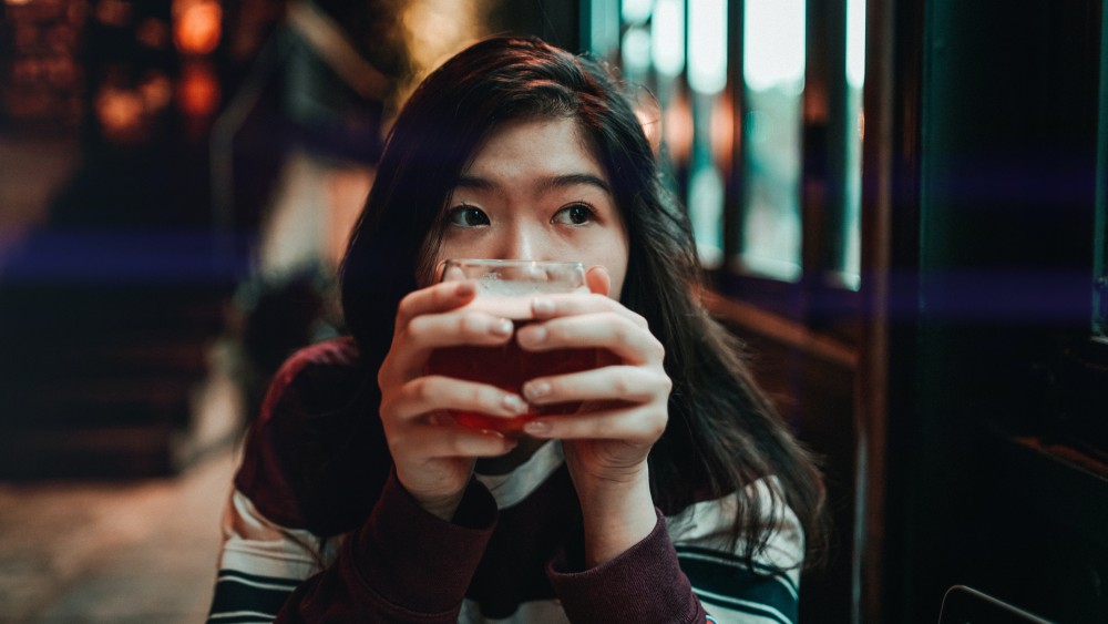 Eine Frau hält ein Glas mit einem Getränk in der Hand und schaut zur Seite.