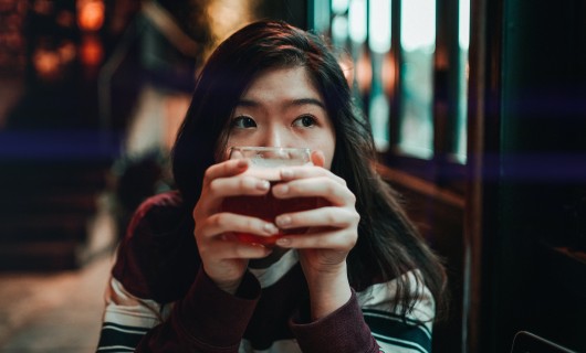 Eine Frau hält ein Glas mit einem Getränk in der Hand und schaut zur Seite.