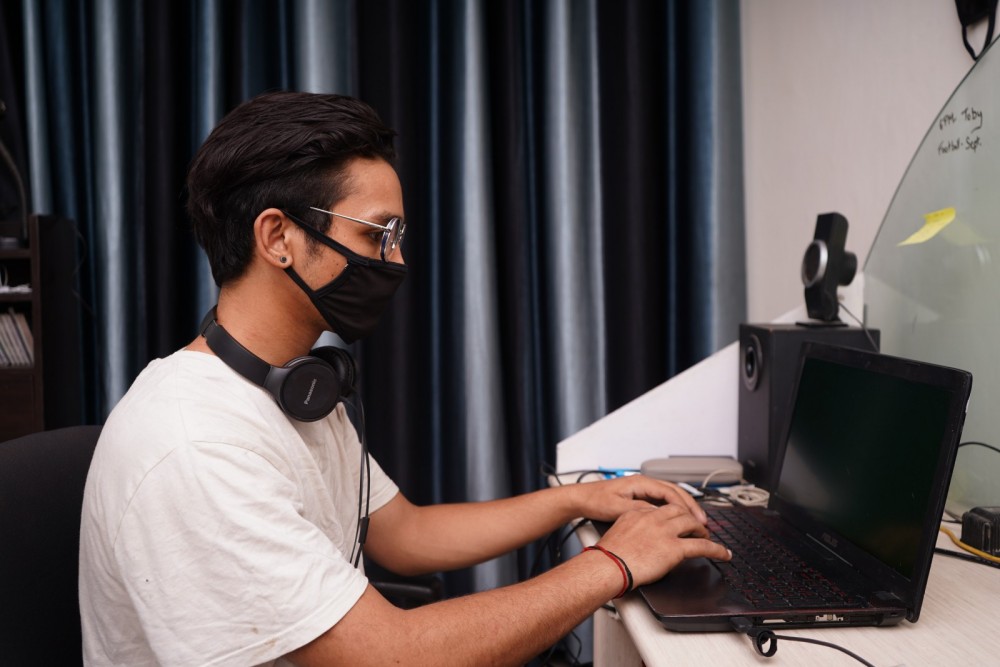 Ein Mann trägt eine Mundnasenmaske und sitzt vor einem Laptop.